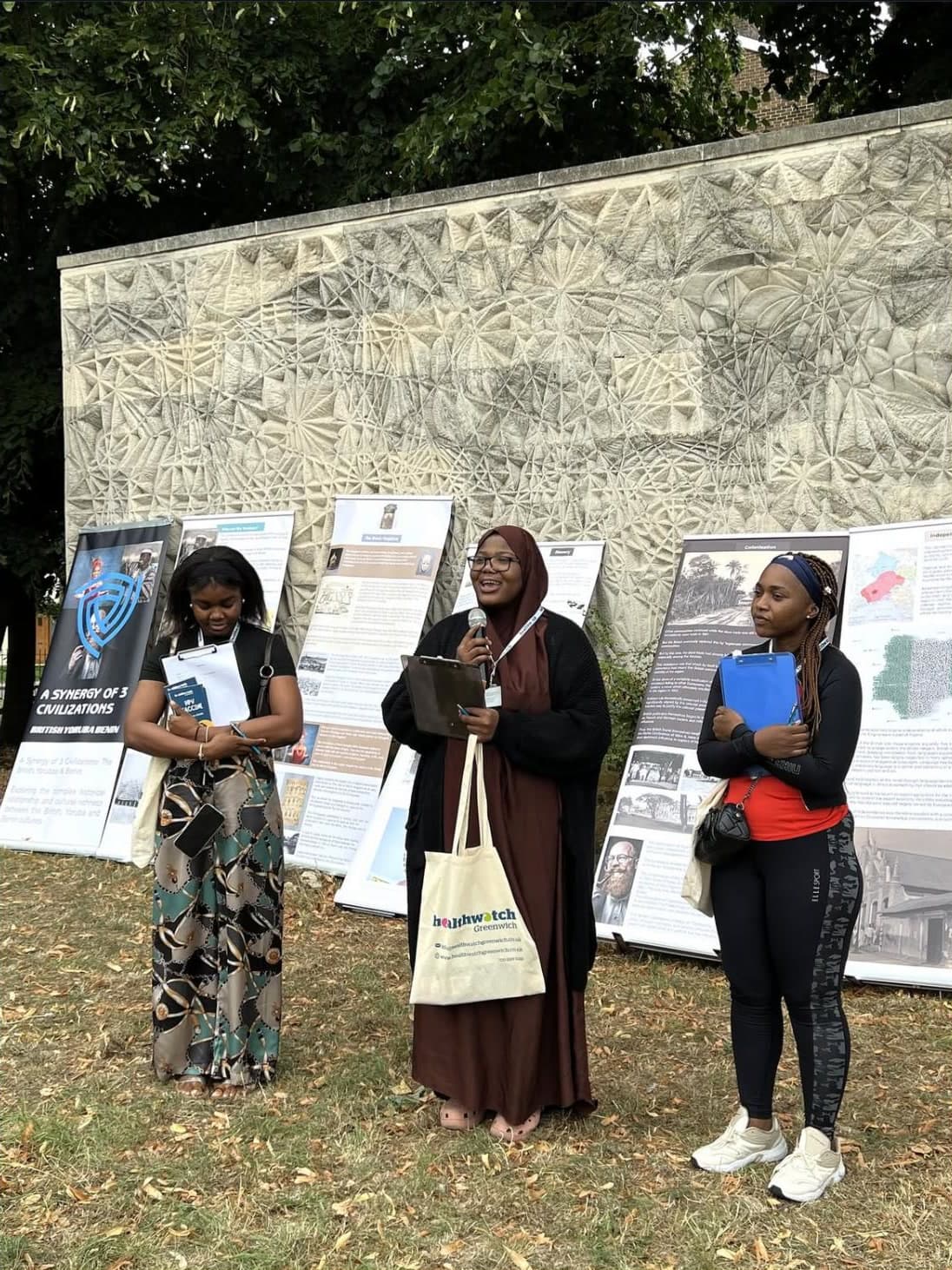 Sofiat, centre, speaking into a microphone at an outdoor community event with Healthwatch Greenwich