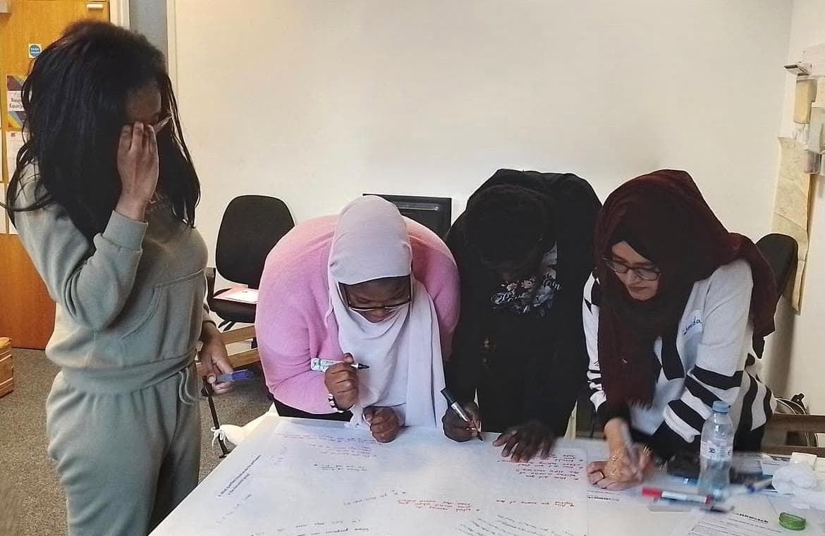 Young women writing ideas on a large sheet of paper during a workshop